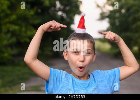 Ragazzo scherza, mette un piccolo cappello di Santa sulla sua testa e punta ad esso con le dita indice. Foto Stock