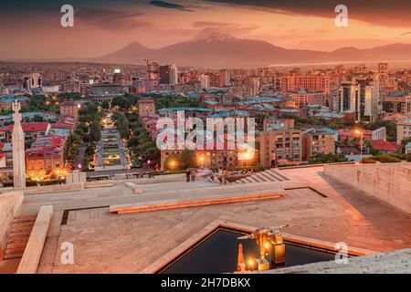 Vista panoramica serale dalle scale del monumento Cascade al colorato tramonto sui tetti della città di Yerevan e simbolo dell'Armenia - Monte Ararat Foto Stock