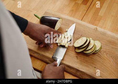 Vista dall'alto da vicino dell'irriconoscibile uomo afro-americano che taglia melanzane mentre cucinano la cena su un tavolo di legno, spazio copia Foto Stock