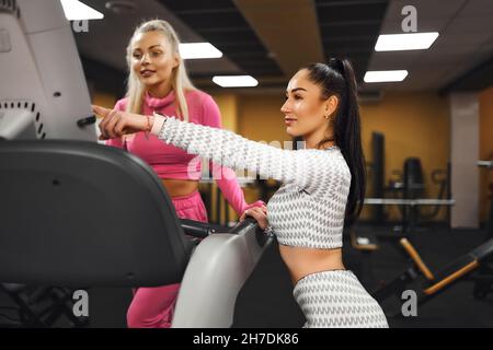 Addestratore personale femminile che aiuta il cliente della donna a usare il tapis roulant in palestra. Formazione personale. Vita sana Foto Stock