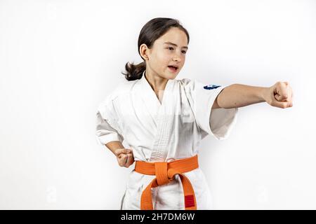 Karate ragazza su sfondo bianco. Una bruna caucasica sportiva ridente in un kimono bianco è impegnato in arti marziali e praticare pugni a mano. Correggi Foto Stock