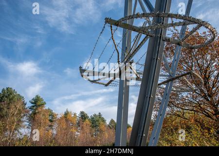 Protezione anti-arrampicata su traliccio di elettricità con filo spinato in giornata limpida con cielo blu e alberi. Foto Stock