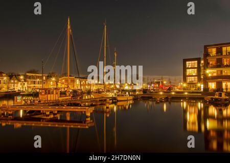 Haarlem, Paesi Bassi, 19 novembre 2021: Vista notturna del fiume Spaarne, con un molo e barche a vela accanto ad un nuovo quartiere residenziale Foto Stock