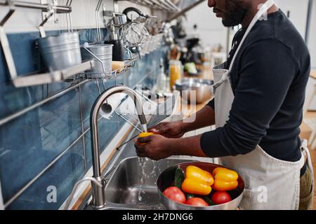Vista laterale ritratto di uomo afro-americano lavaggio verdure fresche durante la cottura in cucina, spazio copia Foto Stock