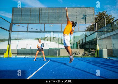 Misto padel match in una corte di erba blu padel - bella ragazza e bell'uomo giocare padel all'aperto Foto Stock