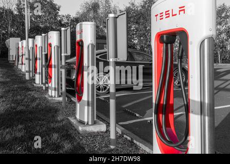 Stazione Supercharger Tesla per la ricarica di veicoli elettrici presso Telford Motorway Services, Shropshire, Inghilterra, Regno Unito. Monocromatico con splash a colori Foto Stock