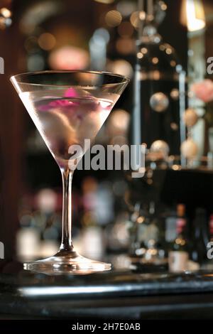 Un cocktail gin guarnito con un'orchidea rosa, servito in un bicchiere martini in un bar Foto Stock