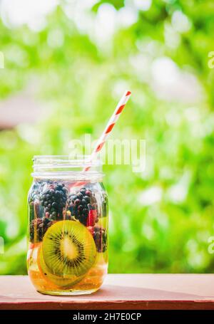 Tè freddo fruttato in un vasetto con tappo a vite con una cannuccia su un tavolo da giardino Foto Stock