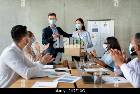 Colleghi multietnici in maschere mediche saluto nuovo membro del team in ufficio Foto Stock