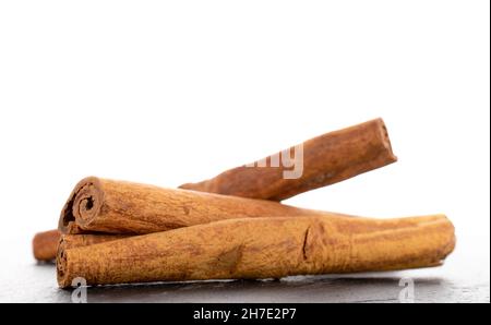Tre bastoncini di cannella secchi fragranti su una pietra ardesia, primo piano, isolati su bianco. Foto Stock
