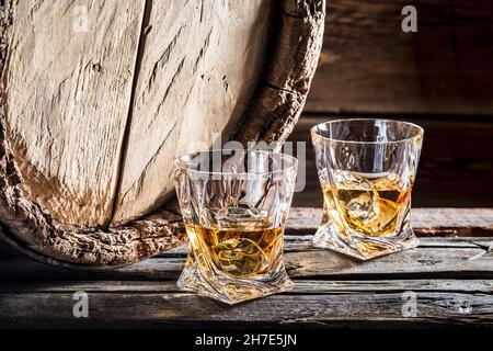 Due bicchieri di whiskey sulle rocce di fronte ad un vecchio barile di legno Foto Stock