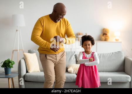 Felice africano americano ragazza piccola e vecchio danzare, divertirsi nel soggiorno interno Foto Stock