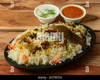 Kashmiri Mutton Gosht o Agnello Biryani preparato in riso Basmati servito con yogurt e sugo di carne su sfondo rustico in legno, fuoco selettivo Foto Stock