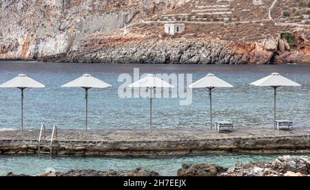 Gerolimenas villaggio a mani Laconia Peloponneso Grecia. Ripide scogliere lastricate piattaforma in pietra con ombrelloni e sedie da spiaggia per rilassarsi nella calma blu se Foto Stock
