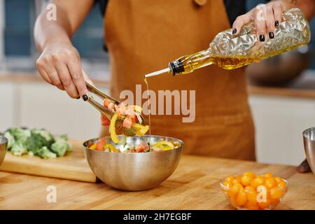 Primo piano di una donna irriconoscibile che aggiunge olio d'oliva all'insalata mentre cucinava la cena in cucina, spazio copia Foto Stock