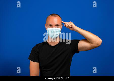 L'uomo concentrato in una maschera medica tiene il dito sul tempio, cercando di trovare una soluzione al problema con la diffusione del virus. Foto Stock