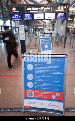 Amburgo, Germania. 18 Nov 2021. Le informazioni su come proteggersi da un'infezione da Corona sono riportate su un poster all'ingresso del checkpoint di sicurezza dell'aeroporto di Amburgo. A seguito di ingenti perdite di milioni di euro dovute alla pandemia di Corona, anche il traffico aereo quest'anno sta subendo un leggero aumento ad Amburgo. Rispetto all'anno pandemico 2020, un maggior numero di aerei decolterà di nuovo da Amburgo nel prossimo inverno, ma il numero di passeggeri è ancora lontano dal livello prima della pandemia di Corona. Credit: Christian Charisius/dpa/Alamy Live News Foto Stock