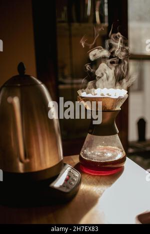 Preparazione del caffè caldo a vapore utilizzando il beccuccio in vetro e il bollitore in acciaio inox con temperatura controllata sul piano di lavoro. La mattina potrai preparare caffè appena fatto. Gocciolamento Foto Stock