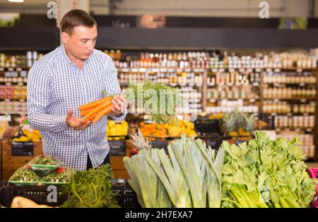 Uomo che sceglie la carota in supermercato Foto Stock