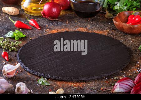 Sfondo culinario con tavola rotonda in ardesia da cucina, olio d'oliva in una brocca e verdure. Spazio vuoto per menu o ricetta con messa a fuoco selettiva Foto Stock