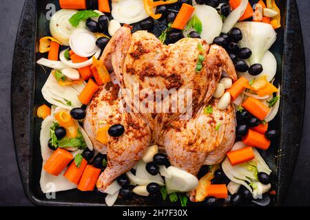 Pollo speziato marocchino crudo con verdure arrosto in una teglie: Pollo crudo con spinotti e finocchio, olive nere, carote, cipolla e aglio Foto Stock