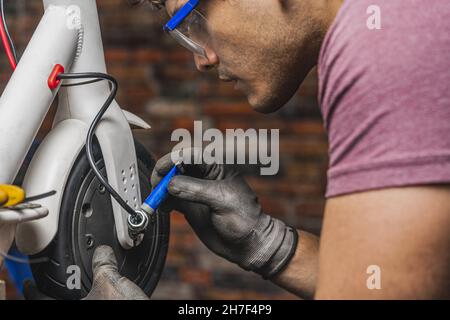 Il meccanico applica una sostanza al meccanismo di cablaggio dello scooter sulla ruota della sua officina Foto Stock