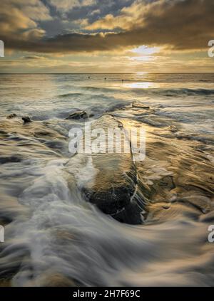 Onde che colpiscono le rocce a la Jolla, California, surfisti dalle sagome Foto Stock