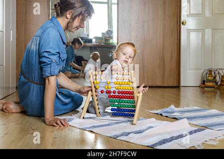 Madre insegnamento bambino piccolo contare su policolore legno di bambola ecologico abaco sul pavimento Foto Stock