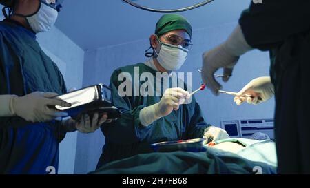 Medico medico chirurgico squadra che esegue la chirurgia paziente, gruppo chirurgo al lavoro in sala operatoria con apparecchiatura di elettrocauterizzazione per l'emero cardiovascolare Foto Stock