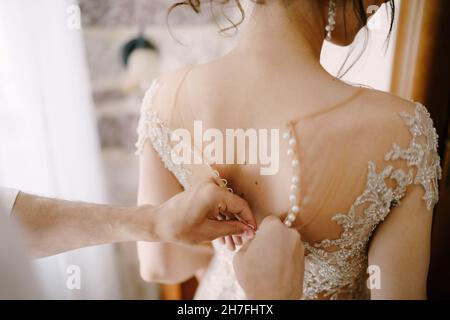 L'uomo stringe i bottoni sul vestito della sposa. Primo piano Foto Stock