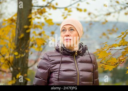 Donna pensierosa con un'espressione lontana all'aperto in autunno in piedi in un parco con foglie gialle colorate sugli alberi che guardano in su Foto Stock
