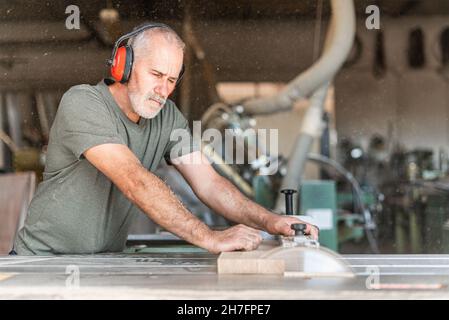 Carpentiere che taglia legno con precisione su una sega da tavolo scorrevole Foto Stock