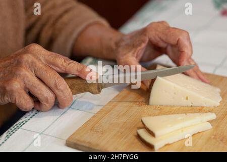 Un primo piano delle mani di una donna anziana affettare un cuneo di formaggio MR - Model rilasciato Foto Stock