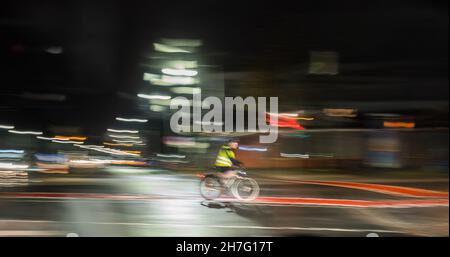 Hannover, Germania. 23 novembre 2021. Una donna biciciclista passa attraverso un incrocio indossando un gilet ad alta visibilità al mattino presto. (Shot with slow shutter speed) Credit: Julian Stratenschulte/dpa/Alamy Live News Foto Stock