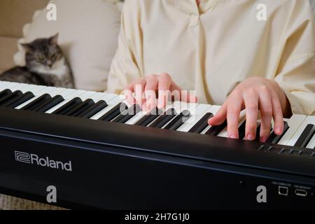 Donna musicista che suona il piano elettronico Roland a casa sul divano in soggiorno - Mosca, Russia, 28 ottobre 2021 Foto Stock