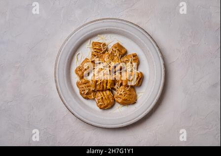 Gnocchi di patate italiani popolari da farina di grano intero, purea di zucca cotta e parmigiano su piastra leggera su sfondo di cemento. Disposizione piatta. Spazio di copia Foto Stock