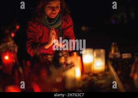 donna di preghiera. Candele nel cimitero. 1 novembre. Festa di tutti i Santi. Hallowmas. Giornata di tutte le anime. Foto Stock