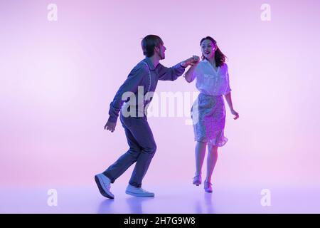 Coppia di ballerini, giovane uomo e donna in abito d'epoca in stile retrò danza danzante swing isolato su sfondo di colore lilla in luce al neon Foto Stock