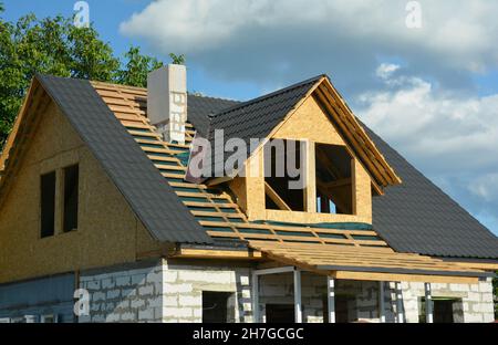 Costruzione di tetti sottotetto. Un primo piano di un tetto in legno che incornicia sopra una barriera al vapore e l'installazione di tegole in metallo, finestre sottotetto, costruzione di camino Foto Stock