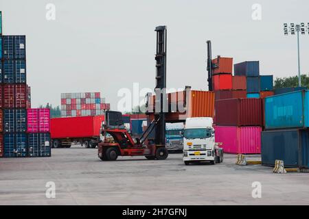 Carrello elevatore a forche di sollevamento del contenitore di carico in cantiere per la spedizione o la dock yard contro Alba cielo con un contenitore di carico in pila in background per i mezzi di trasporto Foto Stock