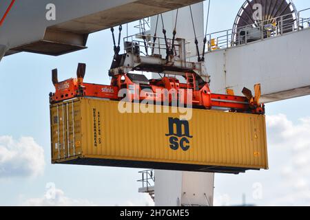 Rotterdam, Paesi Bassi-Aprile 2020: Vista ravvicinata da una gru a portale verso un container marino giallo chiaro sollevato da uno spanditore per ulteriori Foto Stock