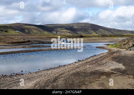 Vista di un'auto a quattro ruote motrici nell'acqua di un fiume in uno degli incroci vicino vulcano Katla su Islanda con montagne sullo sfondo con l Foto Stock