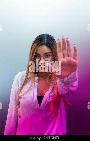Primo piano di donna sorridente con occhiali che mostrano il palmo mentre si trova su sfondo colorato Foto Stock