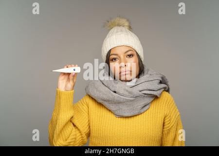 La donna malata in sciarpa mostra termometro soffrire di febbre. Ragazza afroamericana in congedo di malattia Foto Stock