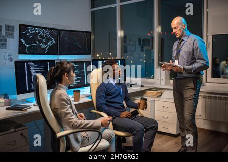 Responsabile maturo e sicuro con tablet che interagiscono con due giovani subordinati durante la presentazione del nuovo progetto Foto Stock