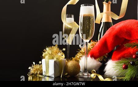 Dettaglio di due bicchieri di vino bianco frizzante e arco dorato e regalo con fondo nero isolato. Vista frontale. Foto Stock