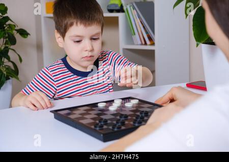 Madre e figlio giocano a dama in casa. Giochi da tavolo per bambini e bambini Foto Stock