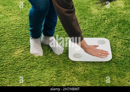 La ragazza misura il peso durante la dieta. Scale intelligenti per la casa. Foto Stock