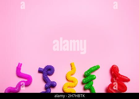 Cinque colorati rosso, viola, rosa, verde, giallo pop tube giocattoli per bambini piegati in diverse forme. Allegro set di giocattoli multicolore antistress in plastica su pi Foto Stock