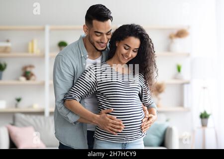 Amorevole marito medio-orientale abbracciando la sua bella moglie incinta Foto Stock